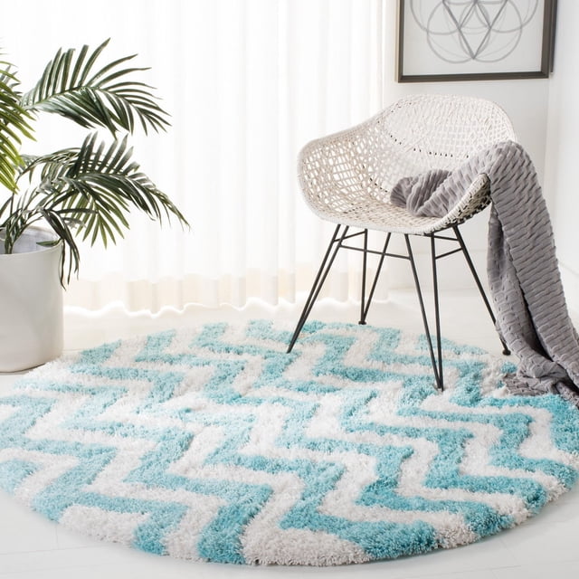 Safavieh Barcelona Carmella Tapis Shag à Rayures en Zigzag, Rond avec Peluche de Poils Longs en Rayures en Zigzag Bleu Pâle et Blanc, Placé sous une Chaise Tissée Blanche avec des Pattes en Métal Noires et un Jeté Tricoté Gris, à Côté d'Une Plante Verte en Pot dans une Pièce Lumineuse avec des Rideaux Transparents, Convient pour Ajouter de la texture et du style aux Zones d'Accent.