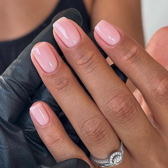 EGNMCR Faux Ongles Press-on Ongles Courts avec Ongles Réutilisables à Coller en 12 Tailles. l'Image Montre une Main avec des Faux Ongles Courts Brillants Bien Appliqués dans une Teinte Rose Douce. les Ongles Sont Tailler à une Longueur Naturelle et Ont une Finition Lisse et Brillante. une Main Noire-Gantée Tient les Doigts, Mettant en Valeur l'Apparence Polie des Ongles. Idéal pour les Fêtes, les Mariages Ou le Port Quotidien, Cet Ensemble Comprend 24 Plaques à Ongles, Colle Gelée, Colle à Ongles, une Lime à Ongles et un Bâton en Bois pour une application et une Personnalisation