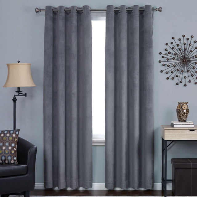 Hometrends Velvet 84" Grommet Blackout Window Curtains Panel in charcoal grey, shown front-facing with soft velvet texture and metal grommet top for easy sliding on curtain rods. Displayed in a living room with a black leather chair, patterned pillow, floor lamp, and side table. These blackout curtains provide privacy, reduce noise, and save energy, ideal for home window coverings.