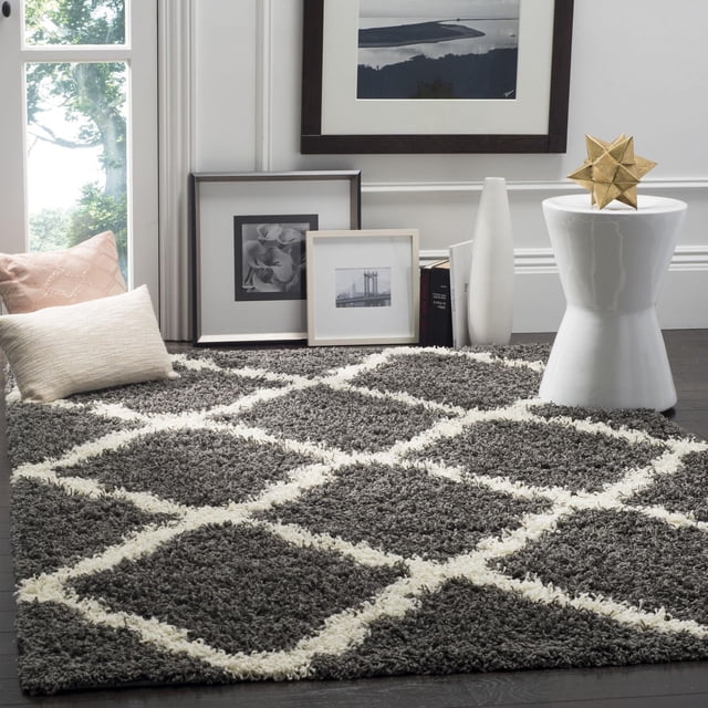 Safavieh Dallas Logan Geometric Shag Area Rug in dark grey with an ivory Moroccan tile pattern, crafted from soft polypropylene for plush comfort, displayed in a bright room with framed black and white photos, neutral pillows, and a white ceramic stool with a gold geometric ornament, ideal for adding texture to living spaces.