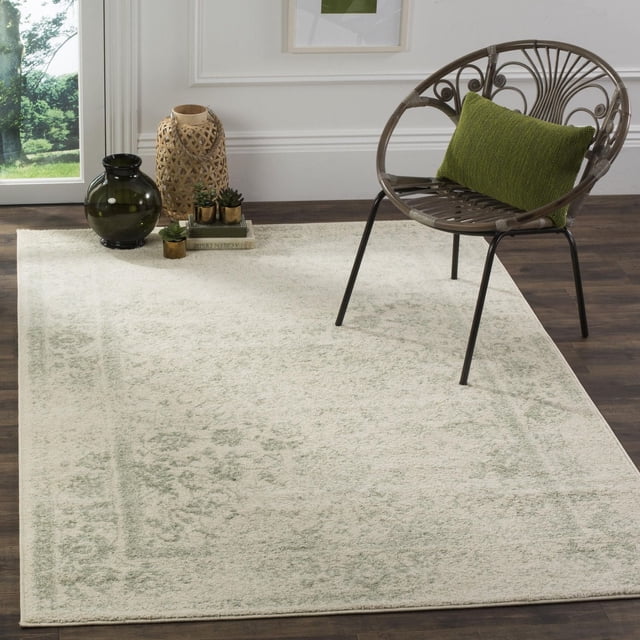 SAFAVIEH Adirondack Wyatt Tapis Traditionnel pour Aire avec Fond Crème Clair et Motif floral Vert Subtil Surteint, Fait de Fils de Polypropylène Durables, Exposé sur un Plancher de Bois Franc Foncé avec une Chaise Ronde en Métal Présentant un Coussin Vert et des vases Décoratifs à Proximité, Convient à la Déco Rustique de Chalet Ou de Ville.