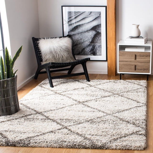 Safavieh Hudson Tapis Shag Géométrique Amias Mettant en Vedette une Peluche Shag Ivoire avec des Motifs Géométriques de Carreaux Gris, Exposé sur un Plancher de Bois Franc Clair dans une Pièce Moderne avec une Chaise Longue Tressée Noire Tenant un Oreiller en Fausse Fourrure Gris et Blanc, une Plante Serpent dans un Panier Tressé, et une table d'Appoint Blanche avec des Façades de Tiroir en Bois et un vase Décoratif, Convient pour Ajouter de la texture et de la Durabilité aux Espaces de Vie à Fort Achalandage.