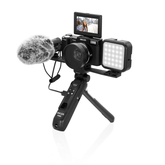 Minolta MND60V 64MP Autofocus 4K60 Ultra HD Vlogging Camera Kit displayed with its accessories, including an external microphone, LED light, wide-angle lens, and tripod with built-in remote control and backup battery. The camera features a flip-out screen displaying a recording, ideal for travel vlogs, tutorials, and social media content creation.