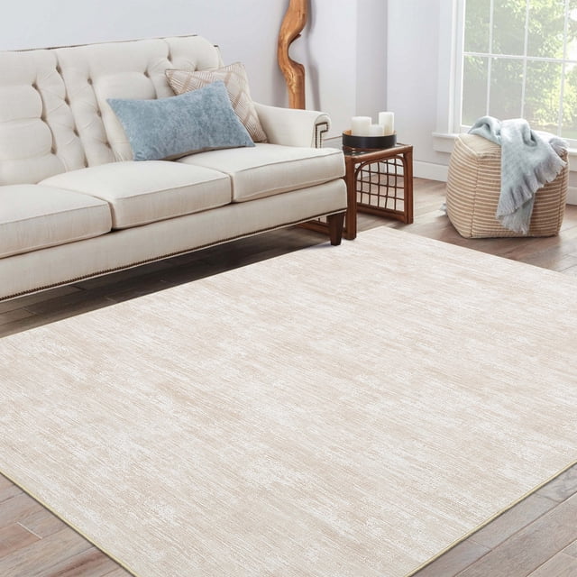 HOMERRY 6' x 9' modern area rug for living room in a solid beige print, displayed in a cozy living room setting with a tufted cream sofa, a wooden side table, and natural light streaming through a window. The rug features a low-pile, soft polyester surface with a non-slip TPR backing, making it safe for high-traffic areas. Its washable and durable design is ideal for pet owners, parents, and renters, complementing modern and neutral decor styles.