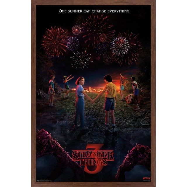 Netflix Stranger Things: Season 3 - Key Art Wall Poster depicting six children standing on a grassy hill at night watching red and white fireworks over a lit town, with the tagline 'One summer can change everything' above and the red Stranger Things 3 logo below, framed in dark wood. This framed poster is suitable for decorating bedrooms, living rooms, or offices.