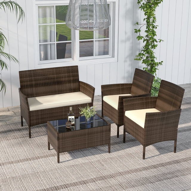 Gymax 4 PCS Patio Rattan Conversation Set with mix brown PE rattan loveseat, two chairs with beige cushions, and a tempered glass coffee table. Ideal for outdoor settings like patios or backyards, displayed on a textured rug with greenery and a white wall backdrop.