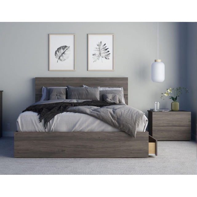 Éléphant Ensemble de Chambre 3 Pcs avec Lit de Rangement Gris Écorce Comprenant Trois Tiroirs sous le Lit sur des Glissières en Métal, une Tête de Lit Effet Planche Rustique et une Table de Nuit Assortie à 2 Tiroirs. le Lit Présente une Literie Grise et des Coussins, Adossé à un Mur Gris Pâle avec Deux Imprimés de Feuilles Encadrés au-Dessus et une Suspension Blanche au-Dessus de la Table de Nuit Tenant un Verre d'Eau et un Petit vase à Fleurs.
