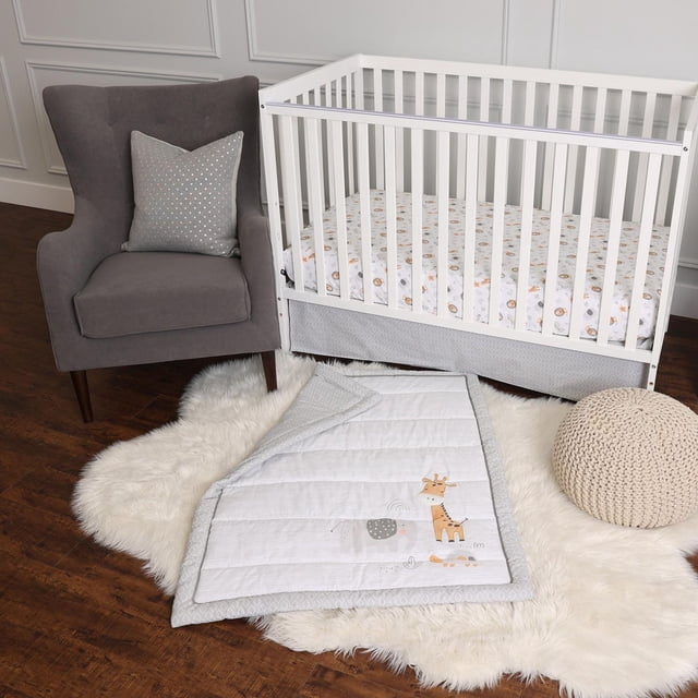 George Baby 3 Piece Crib Bedding Set in grey includes a fitted sheet with pastel animal icons, a matching crib skirt, and a comforter embroidered with a giraffe and elephant, displayed on a white faux fur rug beside a grey armchair with a polka dot cushion and a beige knitted pouf on a hardwood floor in a nursery.
