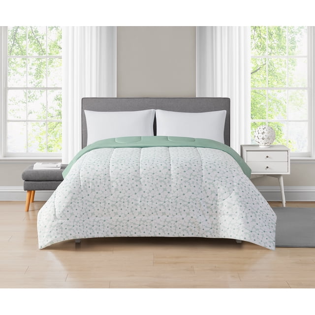 Mainstays Floral Reversible Comforter Twin on a bed with gray upholstered headboard, featuring a white microfiber comforter with green floral print and solid green reversible side, in a bright bedroom with large windows and white curtains, machine washable and suitable for versatile bedroom décor.