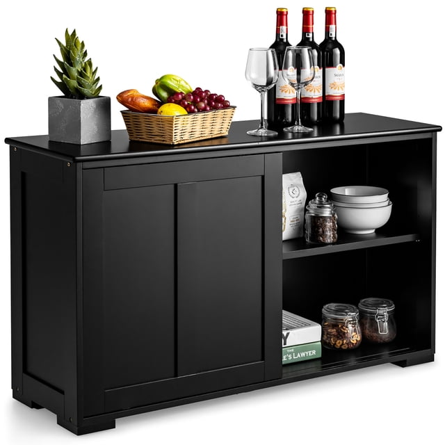 Costway Kitchen Storage Cabinet Sideboard Buffet Cupboard in black wood finish, designed with sliding doors and two spacious shelves for storage. The cabinet top is styled with wine bottles, glasses, a basket of fruits, and a potted plant, while the shelves hold bowls, jars, and books. A versatile storage solution for kitchens, dining rooms, or pantries.