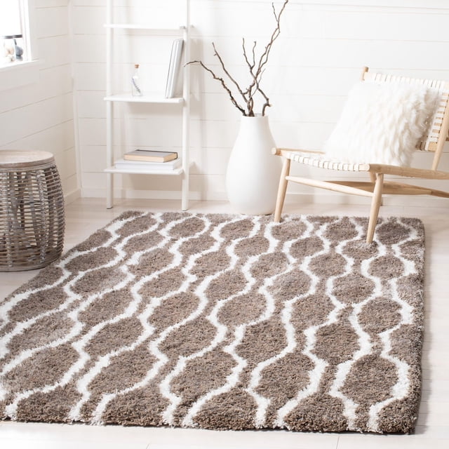 Safavieh Barcelona Melinda Geometric Shag Rug featuring a plush brown and white Moroccan quatrefoil tile pattern on light hardwood flooring, styled with a wooden chair with a white faux fur cushion, a white vase with bare branches, and a white ladder shelf with books, suitable for modern accent rug décor.