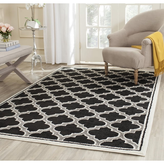 Safavieh Amherst Wilson black area rug with white geometric pattern displayed in a modern living space featuring beige armchair and natural light.