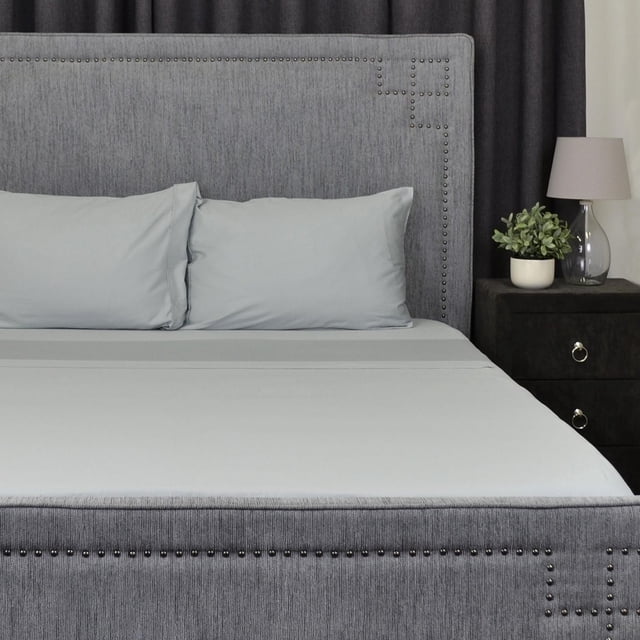 100% Cotton White Sheet Set in grey with 400 thread count cotton fabric, featuring a deep pocket elasticized fitted sheet, flat sheet, and two pillowcases. Displayed on a bed with a grey upholstered headboard with nailhead trim, beside a black nightstand with a lamp and potted plant. The set is ultra soft, durable, easy care, and ideal for comfortable sleep.