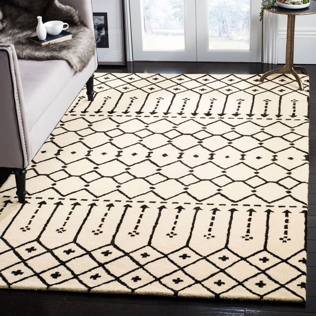 Safavieh Himalaya Darin Geometric Area Rug with cream base and black geometric diamond and linear patterns, crafted from 100% hand-loomed wool, displayed on dark hardwood floor beside a grey upholstered sofa and round side table near glass doors, ideal for modern living spaces.