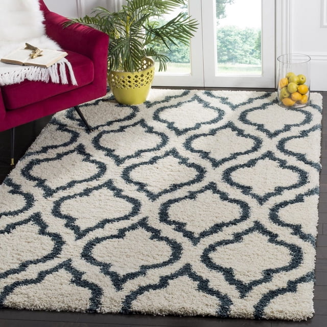 Safavieh Hudson Louise Tapis Shag Géométrique avec une Épaisse pile Shag Ivoire et un Motif de Carreaux Gris Foncé en Forme d'Oignon, Posé sur un Plancher de Bois Franc Foncé à Côté d'Un Fauteuil magenta avec un Jeté Blanc et un Livre Ouvert, Près d'Un Cache-Pot Jaune avec une Plante Verte et un Pot en Verre de Citrons Près d'Une Fenêtre Éclairée par le Soleil, Convient pour Ajouter de la texture aux Espaces de Vie Modernes.