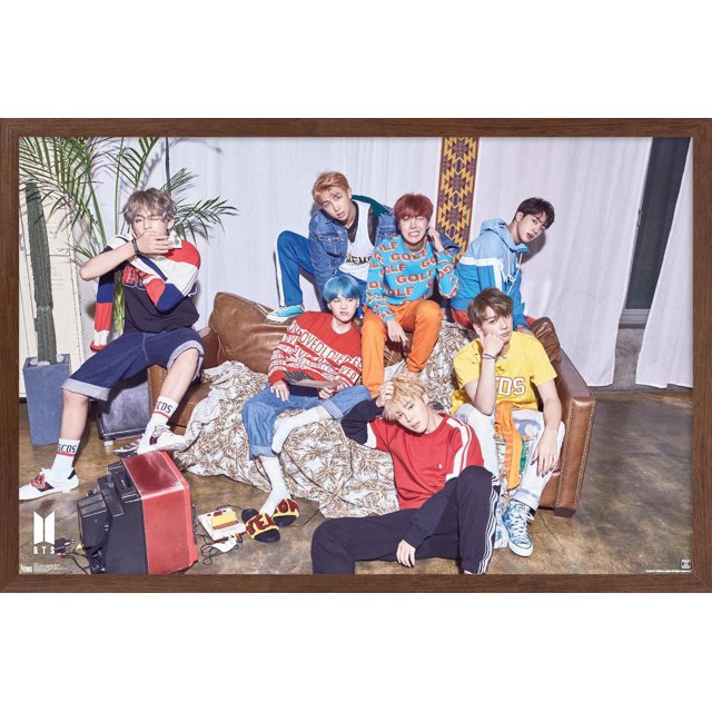 BTS - LOVE YOURSELF ? 'Her' Wall Poster, 22.375" x 34" framed showing seven BTS members in colorful casual streetwear seated and posed on a brown leather couch with a patterned throw, vintage red television, and indoor plants, set against white curtains and a concrete floor, suitable for modern home décor in bedrooms or living rooms.