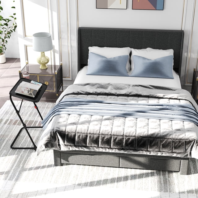 Homy Casa Queen Bed Frame Set with Folding TV Tray Table in grey upholstery, featuring a queen platform bed with two built-in storage drawers and wooden slats, alongside a black adjustable folding tray table holding a magazine and remote, ideal for small bedrooms needing versatile furniture.