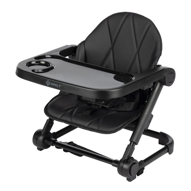Safety 1st Moly Travel Feeding Booster in black with padded seat and adjustable tray featuring cup holder, shown in 3/4 front view on white background, with three height and tray positions, safety harness, and foldable compact frame for easy travel.