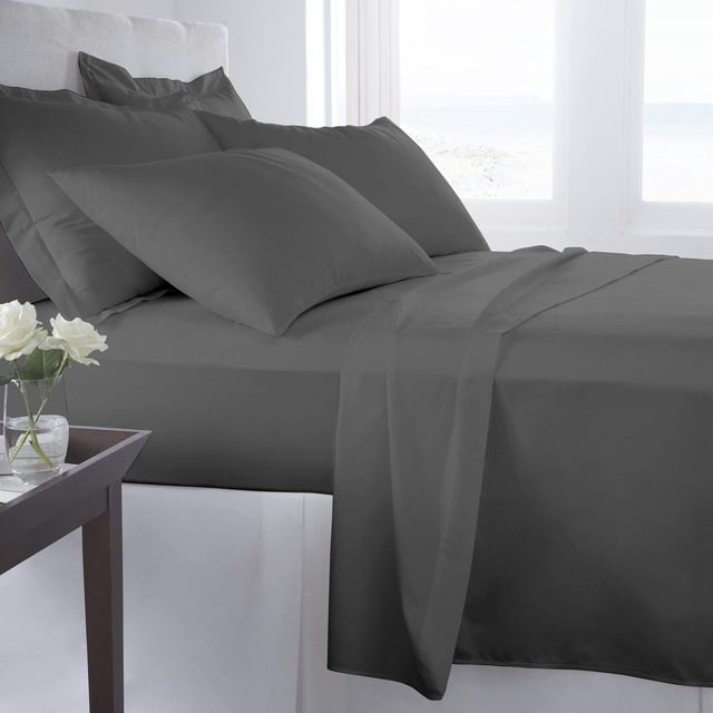 Johnson Home 500 Thread Count Certified Organic Cotton Sheet Sets in dark grey on a bed with white upholstered headboard, including fitted and flat sheets plus pillowcases, featuring breathable, hypoallergenic organic cotton fabric, arranged neatly with a bedside table holding white flowers and a bright window in the background.