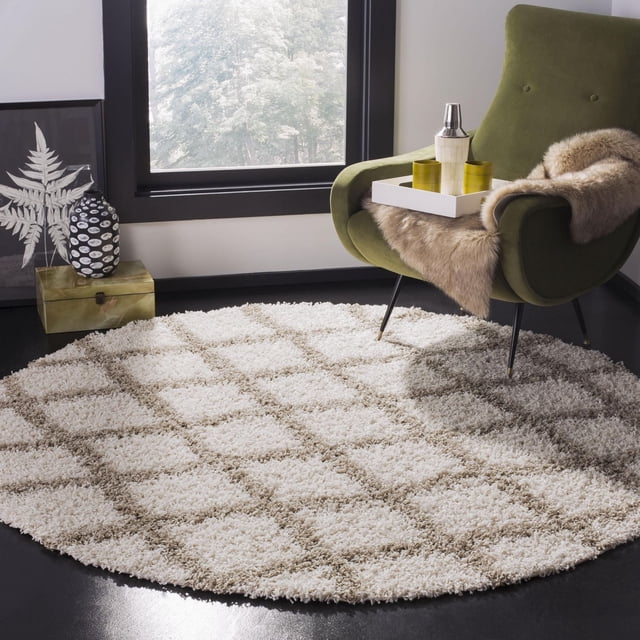 Safavieh Layla Geometric Plush Shag Area Rug, round with a beige and cream diamond pattern, placed on a dark floor beside an olive green armchair with a fur throw and a white tray holding a cocktail shaker and two yellow glasses, near a large window with black trim, suitable for adding texture and warmth to contemporary rooms.