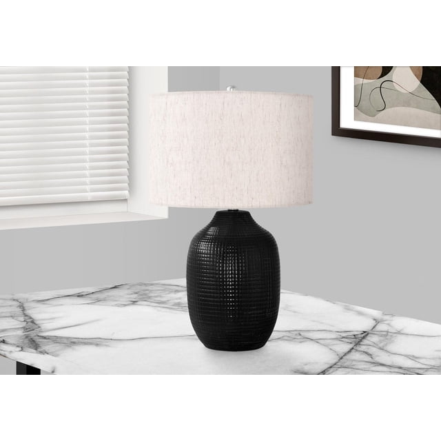 Monarch Specialties Lighting 26"h table lamp with a black glazed ceramic ginger jar base featuring geometric texture and an ivory linen drum shade with silver finial, placed on a white marble table near a window with white blinds and framed abstract art on a gray wall, ideal for adding warm ambient lighting to living rooms or bedrooms.