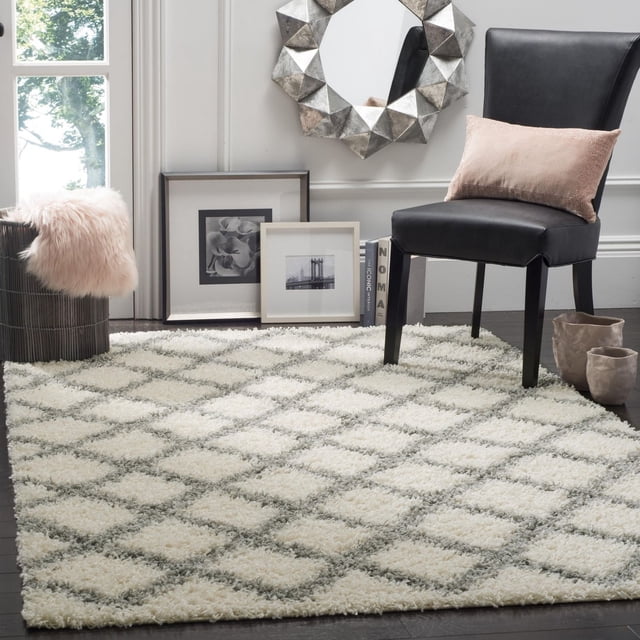 Safavieh Dallas Jerrie Tapis Shag Géométrique Présentant un Motif Losange Pelucheux en Tons Crème et Gris sur Plancher de Bois Franc Foncé. le Tapis en Fibre Synthétique durable Est Style avec une Chaise en Cuir Noire avec un Coussin Rose, des vases Décoratifs, des photos Encadrées Noir et Blanc, et un Miroir Mural Géométrique Argenté, Convient aux Zones à Fort Achalandage à la Maison Ou au Bureau.