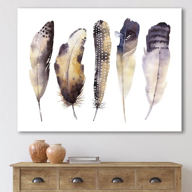 Designart Boho Ethnic Dark Gray Feathers I Canvas Wall Art depicting five vertical watercolor feathers in dark grey, beige, and black with spotted and striped patterns on premium cotton canvas, gallery-wrapped and ready to hang, shown above a wooden sideboard with decorative vases and books, suitable for enhancing bohemian home décor.