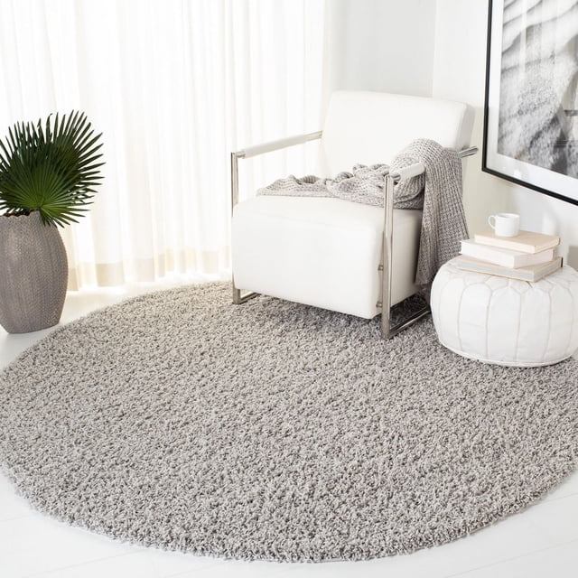 Safavieh Athens Tapis Shag en Peluche Uni en Polypropylène Gris Pâle Rond à Poils Denses et Doux, Placé sous un Fauteuil Moderne Blanc avec Cadre Chromé et Jeté en Tricot Gris, à Côté d'Un pouf Blanc avec des Livres et une Tasse, dans une Pièce Lumineuse avec des Rideaux Transparents et un pot de Plante Texturé, Convient pour Ajouter du Confort Moelleux aux Espaces de Vie.