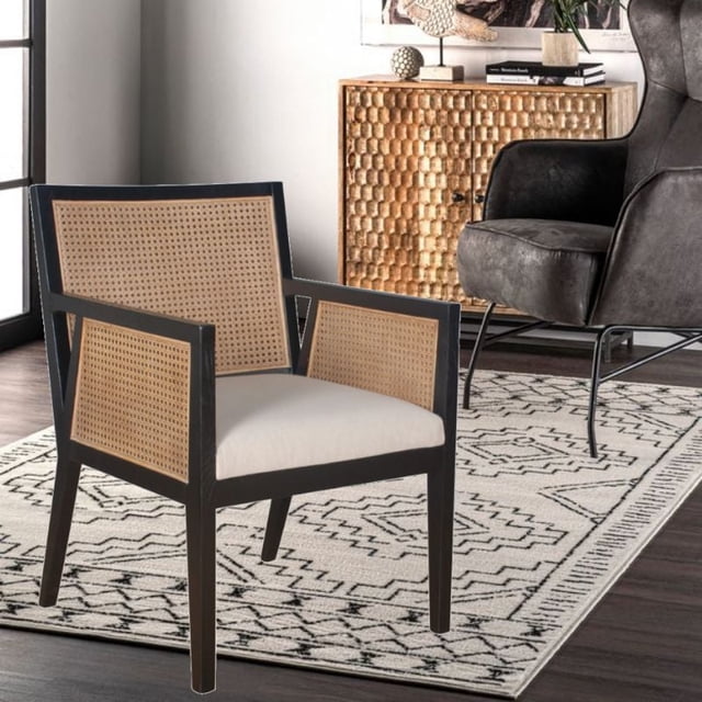 Darnell Dining Chair in Black featuring a solid wood frame with hexagon-patterned rattan cane panels on the back and sides, neutral upholstered seat, and armrests, positioned on a geometric rug in a modern room with a textured wooden cabinet and a dark upholstered armchair.