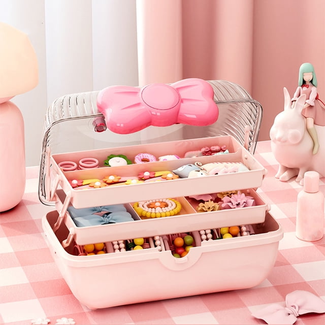 3-Layer Kids Hair Accessories Organizer in pink plastic with a bow-shaped handle and transparent lid. The organizer features three partitioned layers for storing hair ties, clips, and headbands. It is displayed open on a pink checkered surface, showcasing its contents, including colourful hair accessories. Ideal for young girls as a gift for occasions like birthdays or holidays.