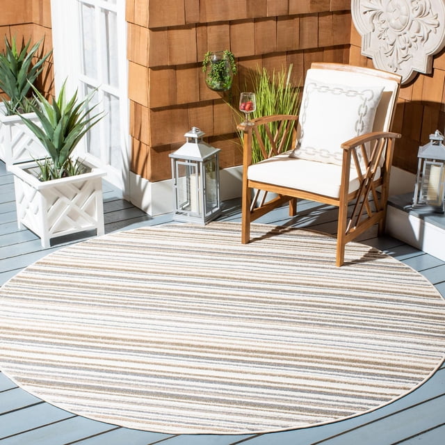 Safavieh Cabana Siomha Striped Outdoor Area Rug, round with beige, white, and light brown horizontal stripes, placed on a light blue wooden deck. Accompanied by a wooden armchair with white cushions, white planters with succulents, and silver lanterns. Designed for outdoor patios, resistant to weather, mold, and fading, also suitable for busy indoor spaces.