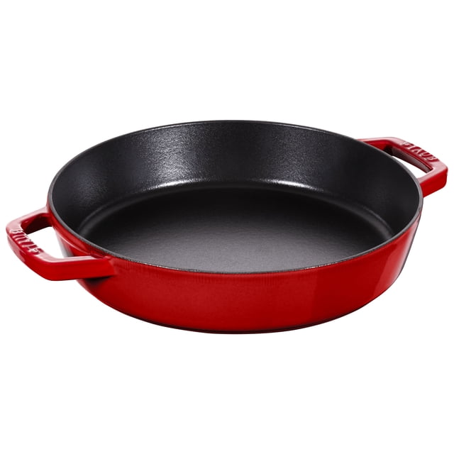 STAUB Pans 26 cm / 10 inch Cast Iron Frying Pan with 2 Handles in cherry red. Ideal for frying, sautéing, and preparing dishes like paella or risotto. Features a matte black enamel interior for enhanced browning and flavour retention. Made from durable enamelled cast iron, suitable for all stovetops including induction, and oven safe up to 500°F. Designed with two loop side handles for easy transfer from stove to table, and often used for serving directly at the table.