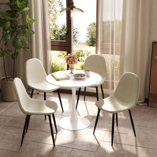 Homy Casa set of 4 modern dining chairs with metal legs and cream fabric upholstery seats arranged around a small white round pedestal table in a sunlit kitchen dining area with large windows and beige curtains. These compact armless chairs feature cushioned seats and sturdy black anti-rust legs, ideal for kitchen seating and small spaces.