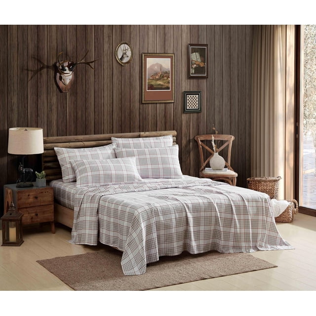 Coleman Printed Polyester Flannel Sheet Set displayed on a wooden bed frame in a rustic bedroom with dark wood panel walls, featuring a white and brown plaid pattern made of soft, warm polyester flannel. The set includes a fitted sheet with deep pockets, flat sheet, and matching pillowcases, all wrinkle resistant and machine washable, styled with a wooden nightstand, lamp, chair with vase, and natural light from a sliding glass door.