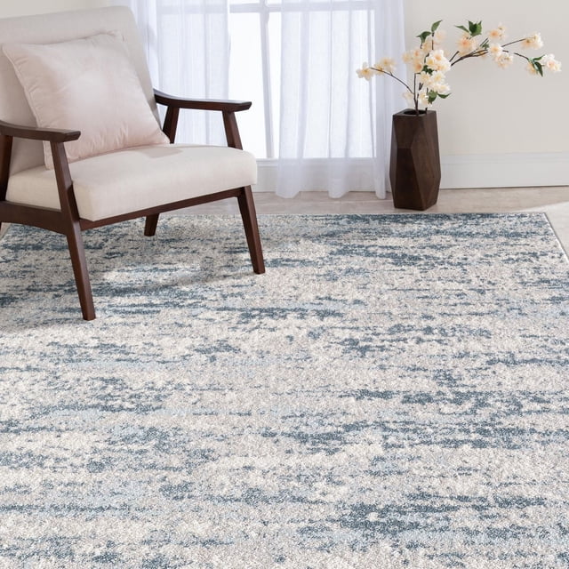 Veruca Tapis Tissé Crème et Bleu avec un design Abstrait Peintre dans des Tons turquoise, Marine, beige et Crème, Fabriqué à Partir de Fils de Polypropylène à Profil Bas pour Résister à la Décoloration et aux Taches, Montré sous un Fauteuil en Bois Rembourré beige et à Côté d'Un vase Géométrique Foncé Tenant des Fleurs de Pêche dans une Pièce Légèrement Éclairée avec des Rideaux Blancs Transparents, Convient aux Salons, aux Salles à Manger Ou aux Chambres.