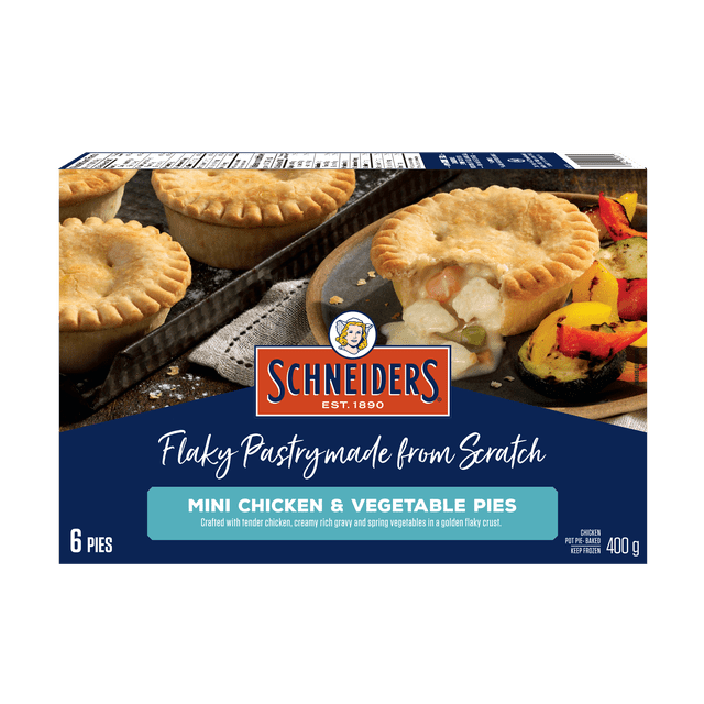 Schneiders Mini Chicken & Vegetable Pies package showing six golden flaky mini pies, one cut open revealing creamy chicken, peas, and carrots filling, served with grilled spring vegetables, highlighting frozen meat pies made with premium chicken and rich gravy in a flaky crust.