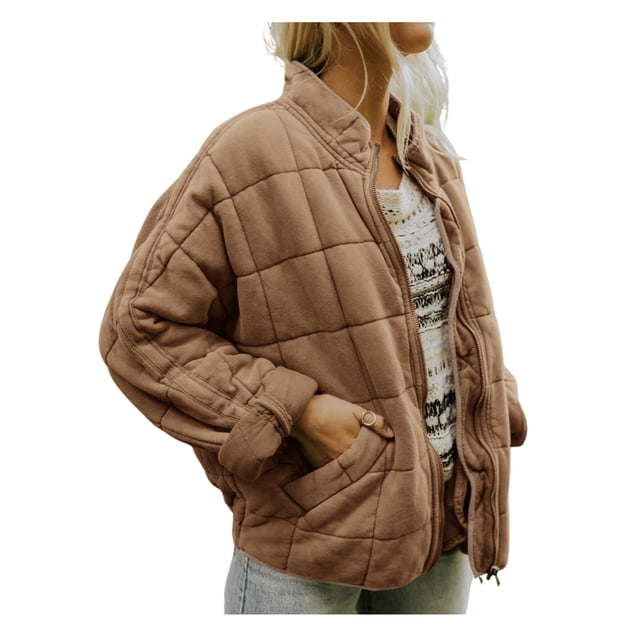 Kmbangi Women Stand Collar Long Sleeve Solid Color Full Zip Quilted Jacket in a light brown tone. The jacket features a stand collar, long sleeves, and a quilted design with a full zip closure. It includes side pockets and a loose fit, ideal for casual wear during colder seasons. The model pairs it with a patterned sweater and light-wash jeans.