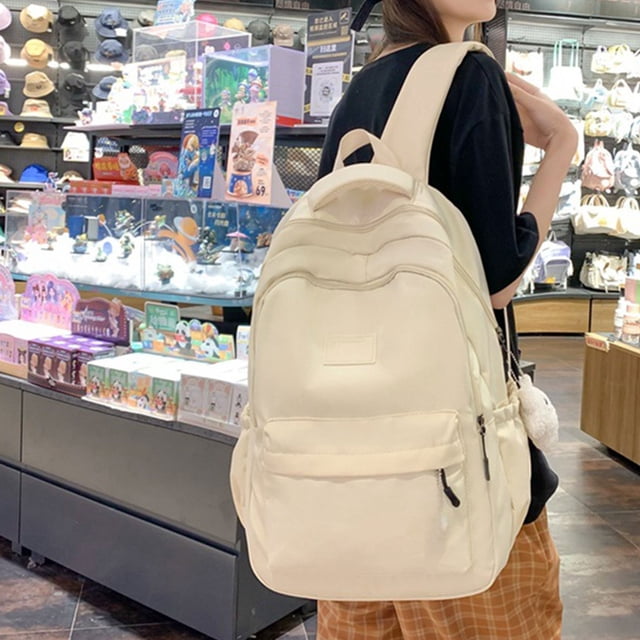 ZZkhGO Large Capacity Backpack for Women, a stylish campus bag in a solid light color, featuring a spacious main compartment, two front pockets, and two side pockets for organized storage. The backpack is worn by a person in a casual retail environment, showcasing its padded shoulder straps for comfort and sturdy construction for durability. Ideal for college students, adult backpacks, and versatile for school or travel use.