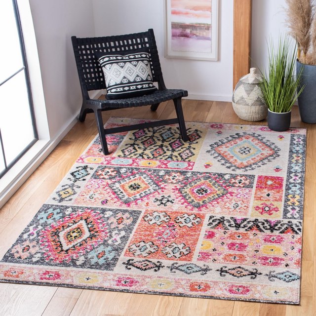 SAFAVIEH Montage Anuki Southwestern Outdoor Area Rug displaying a patchwork of southwestern geometric patterns in muted pink, orange, blue, and beige tones, power-loomed with durable synthetic yarns resistant to water, mold, and fading, laid on a light wood floor beside a black woven chair with a patterned cushion, near potted plants and a woven basket, suitable for outdoor patios or sunrooms.