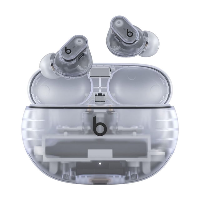 Beats Studio Buds + True Wireless Noise Cancelling Earbuds with translucent smoky grey earbuds and white silicone tips, displayed above a matching transparent charging case showing internal circuitry and the black Beats logo, designed for active noise cancelling and wireless Bluetooth connectivity.