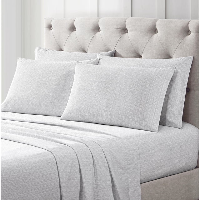 Nicole Miller Studio 6 piece Ella Printed Sheet Set in grey chevron pattern on a bed with a beige tufted headboard, including 4 pillowcases, flat sheet, and deep pocket fitted sheet designed for mattresses up to 16 inches deep, made of 60% cotton and 40% polyester with 250 thread count.