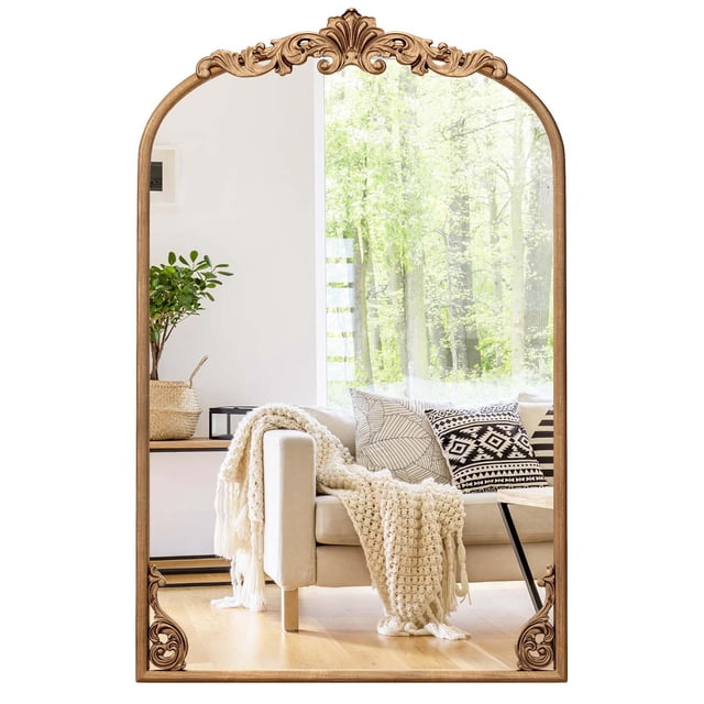 Costway 30" x 20" gold traditional vintage ornate baroque arched mirror for wall with metal frame. The mirror features intricate baroque patterns on the arched frame, finished in a luxurious gold tone. It is displayed in a bright living room setting, reflecting a cozy interior with a beige sofa, patterned cushions, and a knitted throw. Designed for entryways, living rooms, or bathrooms, it includes welded hanging hooks for secure installation and offers a high-definition reflection.