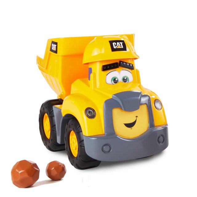 Cat® Junior Crew Construction Buddies Dump Truck interactive preschool toy in bright yellow with gray front bumper and animated smiling face wearing a CAT helmet, featuring large black wheels and two brown play rocks beside it, designed for ages 2 and up.