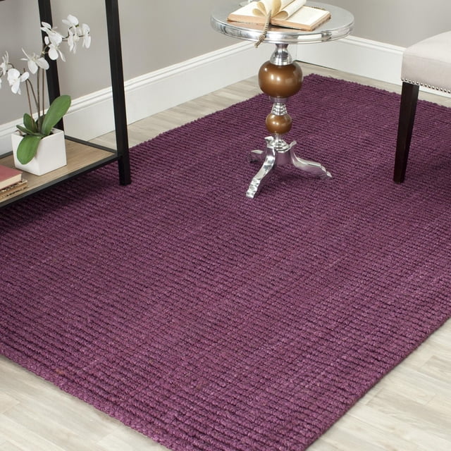 Safavieh Natural Fiber Levi Braided Area Rug in a natural purple tone with a durable braided texture, set on light wood flooring with a silver and brown side table and white orchid plant, ideal for coastal or casual beach house style interiors.