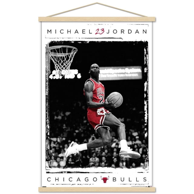 Michael Jordan - Dunk Wall Poster, 14.725" x 22.375" Framed showing Michael Jordan in a red Chicago Bulls jersey number 23, captured mid-air holding a basketball near the hoop with a black and white crowd background and white border, suitable for sports-themed room decor.