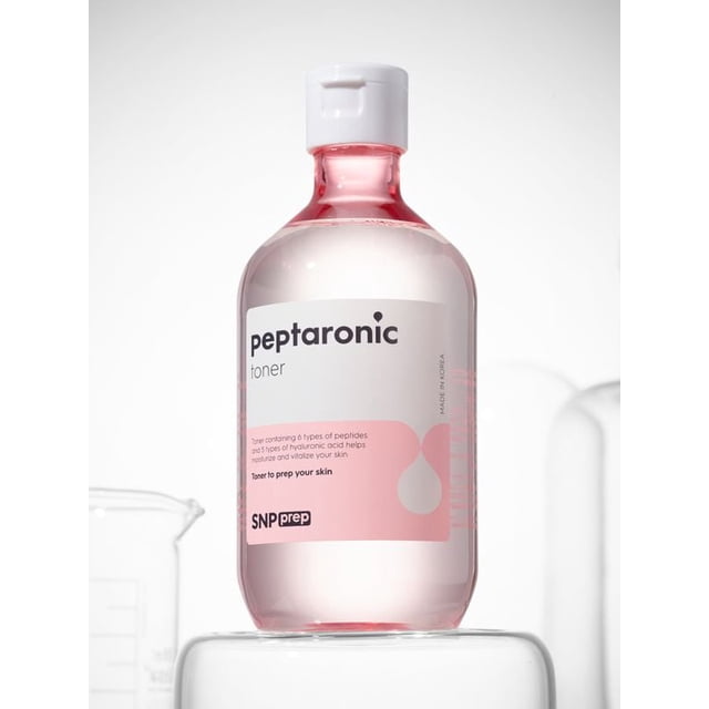 SNP Prep Peptaronic Toner 320ml in a clear plastic bottle with a white flip cap, featuring a pink and white label that highlights its formula with 6 types of peptides and 5 types of hyaluronic acid to moisturize and vitalize skin, displayed on a clear pedestal against a white background with a faint beaker silhouette, suitable for prepping skin in facial skincare routines.
