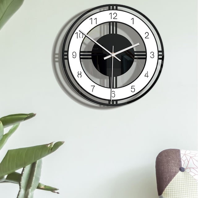 TIMIFIS Wall Clock Style Wall Clock Silent Transparent Acrylic Clock for home and living room. The clock features a modern design with a transparent acrylic face, black and white accents, and clear numbering. It is mounted on a light-colored wall, with part of a plant and a patterned cushion visible in the foreground. Suitable for living rooms, bedrooms, or offices.