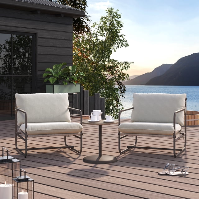HOMETRENDS Augusta Steel 3-Piece Outdoor Chat Set with Cushions, Grey, featuring two rust-resistant powder-coated steel chairs with grey UV-resistant cushions and a round all-season steel table with faux wood finish, set on a wooden patio deck overlooking a lake and mountains, ideal for outdoor seating and casual conversation.