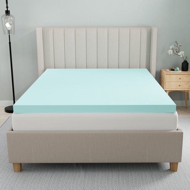 Dream Serenity® 2.75-inch Gel-Infused Memory Foam Mattress Topper - D in light blue gel foam on a white mattress with a beige upholstered bed frame featuring vertical channel tufting. The breathable, pressure-relieving topper supports all sleep styles and is shown in a bedroom with a wooden nightstand and black floor lamp.