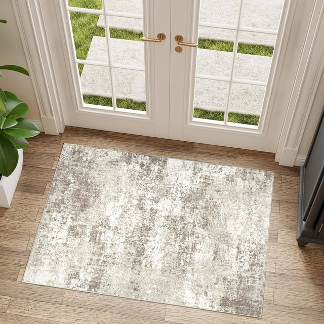 BERTHMEER 2'x3' small abstract area rug in beige, displayed in an entryway with wooden flooring and glass doors. The rug features a neutral abstract design with low-pile polyester and thermoplastic rubber material for durability and non-slip functionality. Ideal for indoor use, this washable rug is machine washable and easy to maintain.